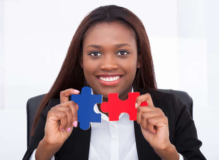 Portrait of confident businesswoman holding puzzle pieces in officeの写真素材