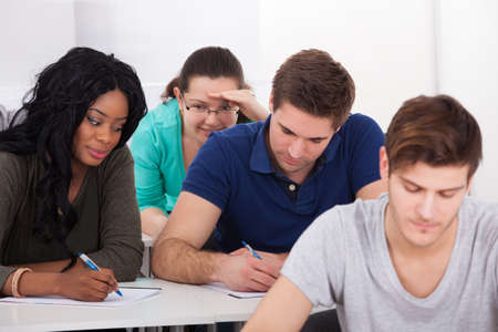 Female college students trying to cheat from male classmate during test in classroom