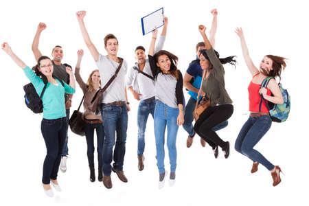 Full length portrait of successful university students with arms raised jumping over white...