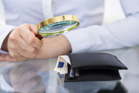Close-up Of Businessperson Holding Magnifier Over  Money Walletの写真素材