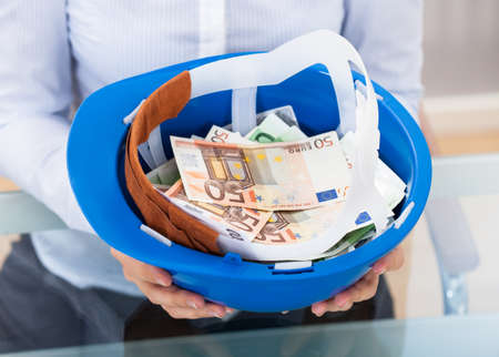 Businessperson Holding Blue Hardhat Full Of Euro Banknotesの写真素材