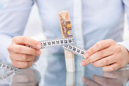 Close-up Of Businessperson Holding Measuring Tape Around An Euro Banknoteの写真素材