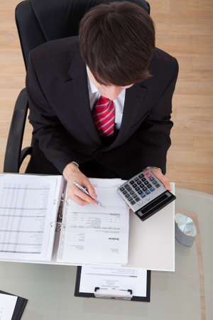 High angle view of confident businessman calculating finance using calculator at desk in officeの写真素材