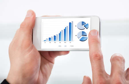 Man looking at a graph on his mobile phone as he accesses data stored in the cloud or onlineの写真素材