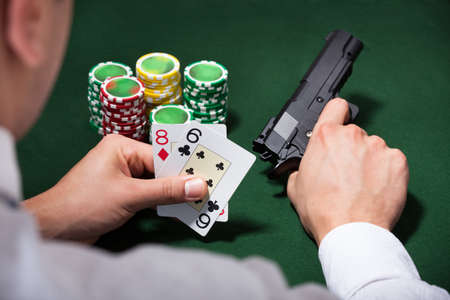 Rear view of man playing poker while holding gun in casinoの写真素材