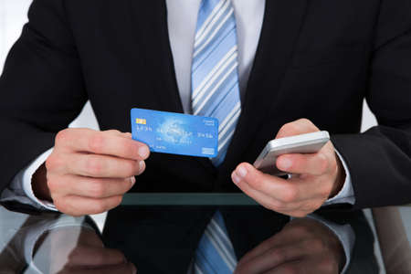 Businessman doing online banking or making a purchase through an online store using his dank credit card  and a mobile phone close up view of his handsの写真素材