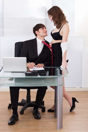 Young undressed businesswoman pulling lusty boss towards self in officeの写真素材