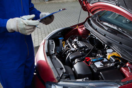 Midsection of mechanic holding clipboard in front of open car engine at streetの写真素材