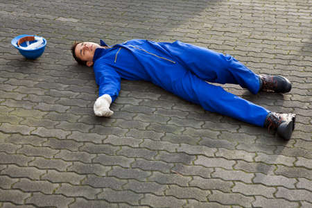 Full length of young unconscious repairman in uniform lying on streetの写真素材
