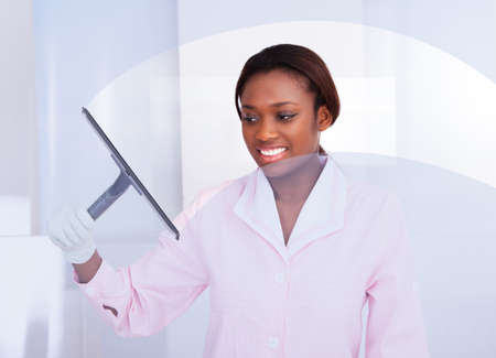 Smiling African American housekeeper cleaning glass in hotel