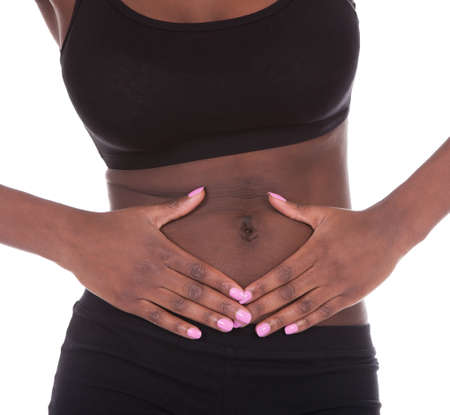 Young African American woman in undergarments suffering from stomachache against white backgroundの写真素材