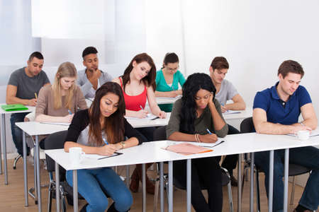 Group of multiethnic college students writing at desk in classroomの写真素材