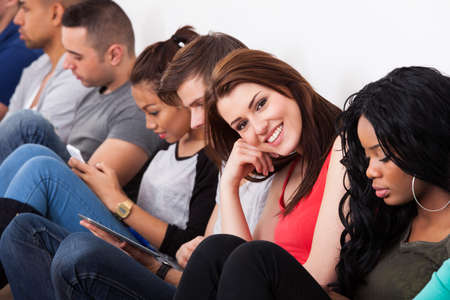 Portrait of beautiful college student sitting with classmates against wall in classroom