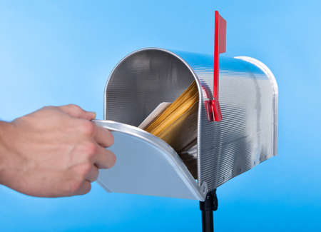 Man opening his mailbox to remove mail inside  close up of his hand on the open door against a blue...
