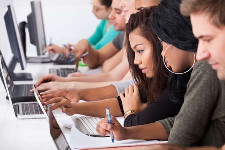 Female college students using laptop at desk in computer classの写真素材