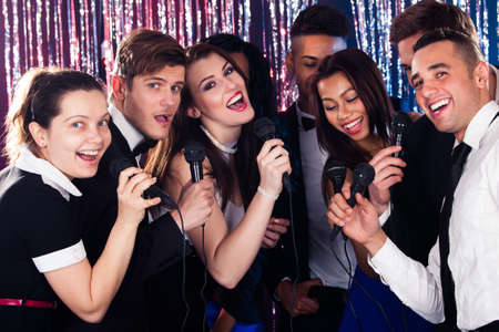 Portrait of happy multiethnic friends singing into microphones at karaoke partyの写真素材