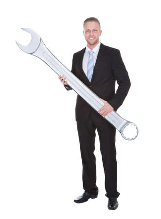 Handsome bearded businessman in a smart suit holding a large metal spanner in his hands conceptual of problem solving  isolated on whiteの写真素材