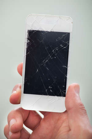 Businessman holding a damaged smartphone with a smashed screen in his hand displaying it to the...