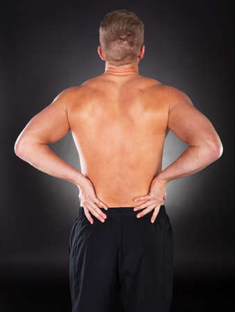 View from behind of a shirtless strong muscular man with backache clutching his lower back with his handの写真素材