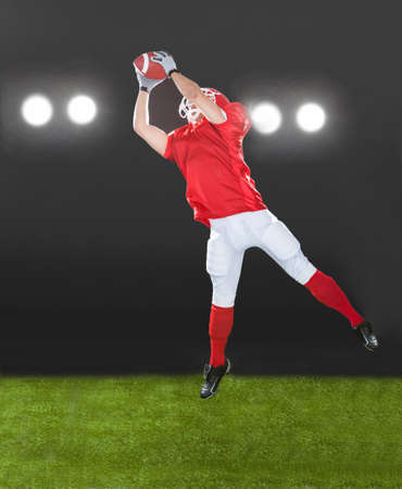 Full length of American football player jumping on field at nightの写真素材