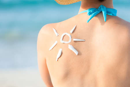 Rear view of young woman with sun drawn from sunscreen on back at beach