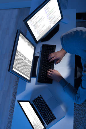 Side view of hacker using multiple computers to steal data at table