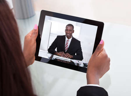 Cropped image of businesswoman attending video conference with colleague on digital tablet at desk in officeの写真素材