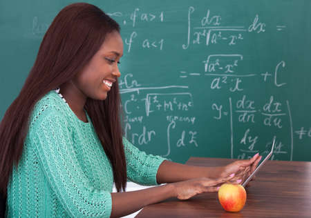 Portrait of confident female teacher holding digital tablet at school desk