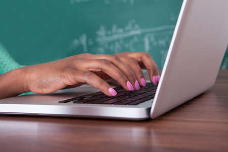 Cropped image of female teacher using laptop at classroom desk