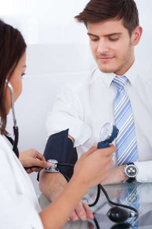 Female doctor checking businessman's blood pressure at desk in clinicの写真素材