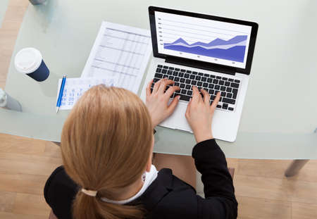 High Angle View Of Businesswoman Using Laptop At Office Desk