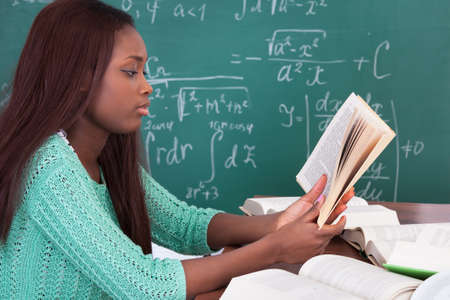 Side view of African American teacher reading book at classroom desk