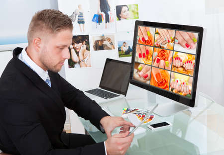 Businessman sitting at his desk in front of a large screen monitor editing photographs