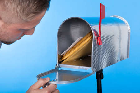 Man opening his mailbox to remove mail inside  close up of his hand on the open door against a blue skyの写真素材