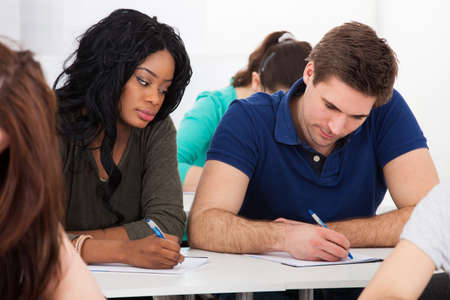 Portrait of male college student sitting at desk with classmates in backgroundの写真素材