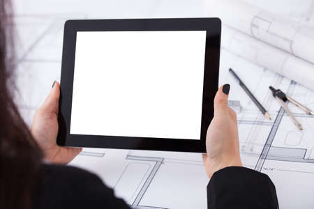Over the shoulder  view of architect woman with digital tablet and blueprint at desk in office
