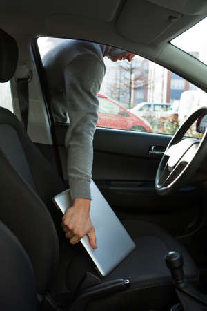 Cropped image of thief stealing laptop through car window