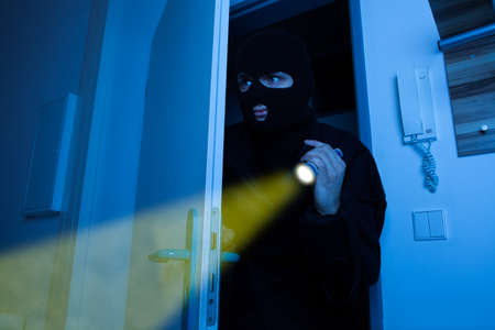 Thief holding flashlight while secretly entering into houseの写真素材