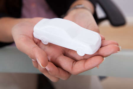 Cropped image of business people holding toy car together in officeの写真素材