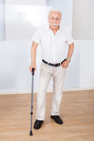 Full length portrait of disabled senior man with walking stick standing at nursing homeの写真素材