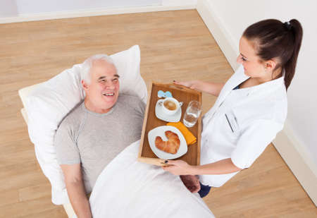 Young female doctor serving breakfast to senior man in hospitalの写真素材