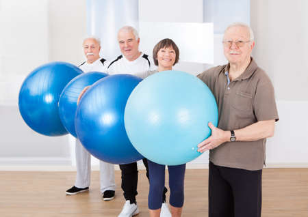 Portrait of confident senior people carrying fitness balls at healthclubの写真素材