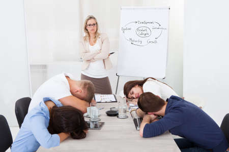 Angry businesswoman looking at tired colleagues sleeping during presentation in office
