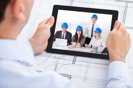 Cropped image of male architect video conferencing with team through digital tablet in officeの写真素材