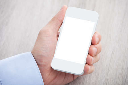 Closeup of businessman's hand holding cellphone with blank screen on desk