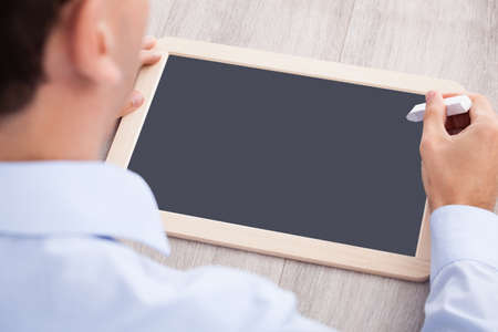 Cropped image of businessman with slate and chalk at desk in officeの写真素材