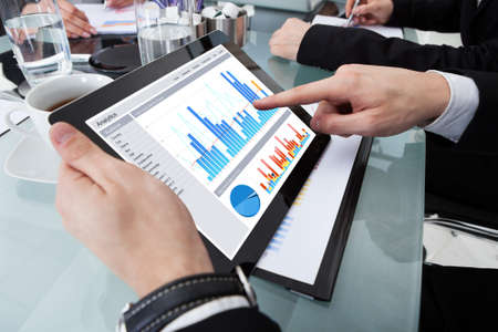 Cropped image of businessman using digital tablet with colleagues at desk in office