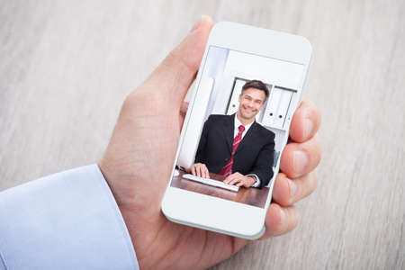Cropped image of businessman video conferencing with colleague at deskの写真素材