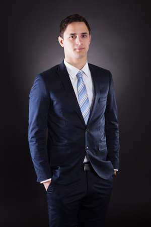 Portrait of confident businessman standing with hands in pockets against black backgroundの写真素材