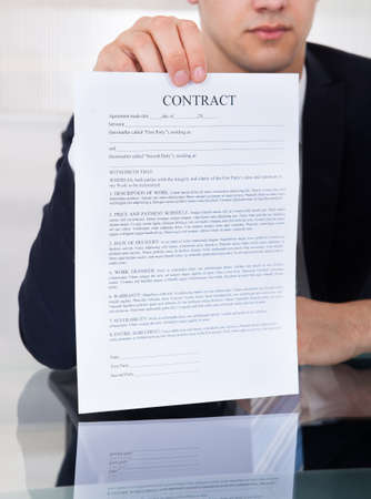 Midsection of businessman showing contract paper at desk in officeの写真素材